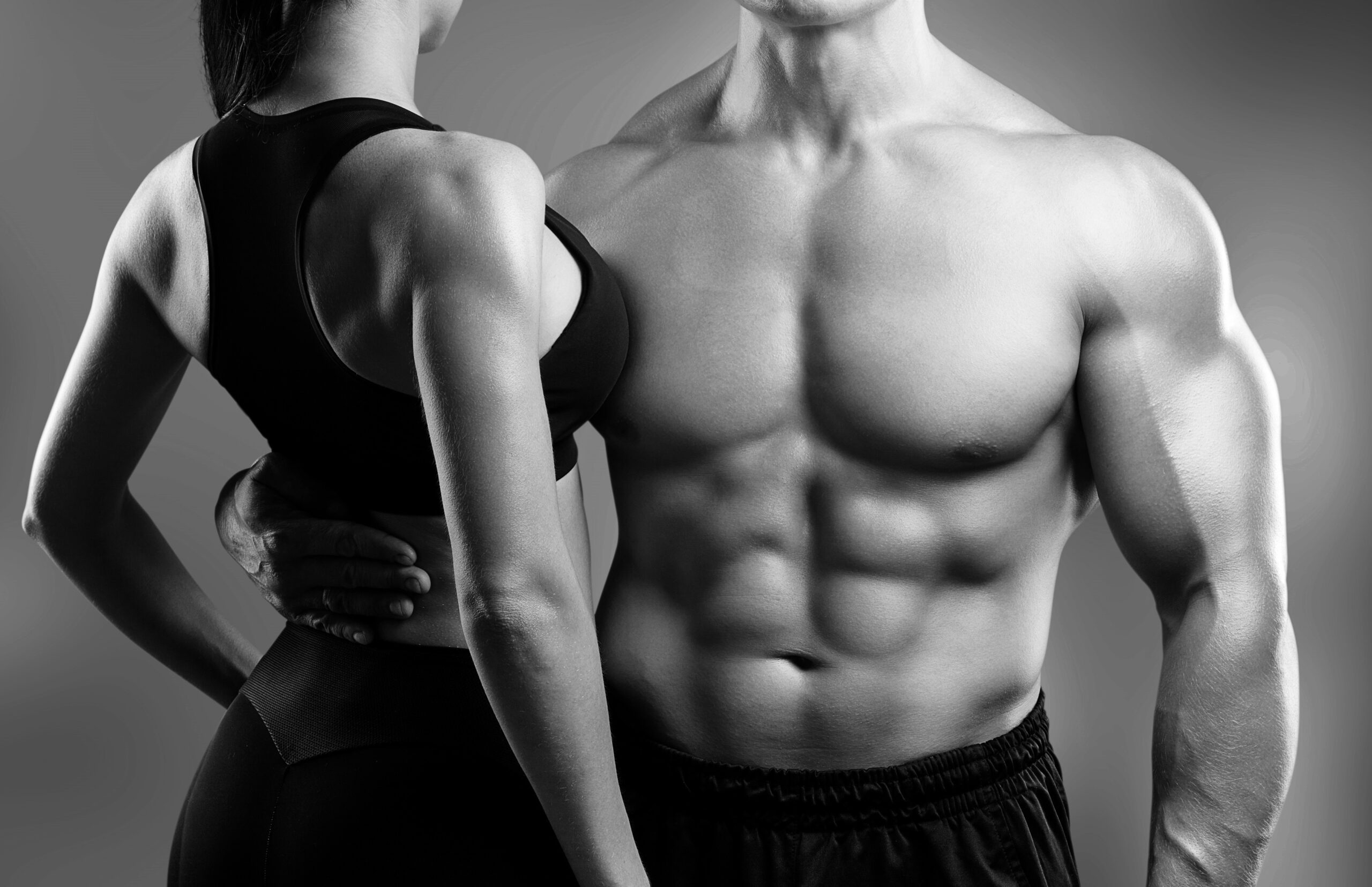Back view of a shirtless man and a woman in a black sports top, both showing toned shoulders and torso against a gray background.